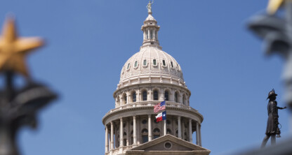 The Texas State Capitol building with the U.S. and Texas flags, viewed through a decorative fence with gold stars, under a clear blue sky—a striking view for visiting Chicago lawyers or any corporate law office professional.
