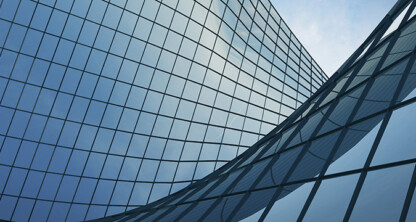 Curved glass facade of a modern building reflecting the sky, with grid-like window patterns and a blue tint—an impressive setting for prestigious law offices specializing in intellectual property law.