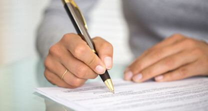 A person holding a pen signs a document on a glass table, with focus on the hand and signature area—depicting how chicago lawyers provide crucial litigation support for their clients.