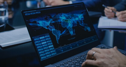 A person at a corporate law office uses a laptop displaying a digital world map with network connections in a meeting room; others are taking notes in the background.