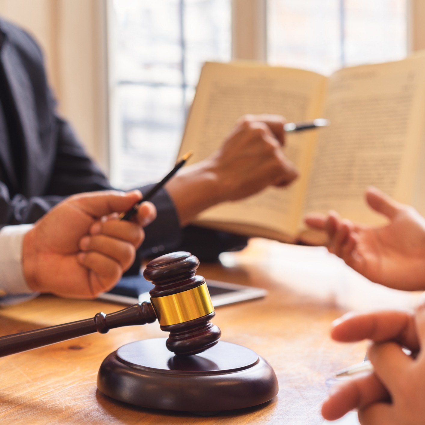 A close-up of hands in a legal meeting with chicago lawyers, a gavel on the table, an open book, and people discussing intellectual property law with pens in hand.