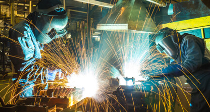Two workers in protective gear weld metal, producing bright sparks and intense light, much like the expertise found in a corporate law office handling complex legal matters.