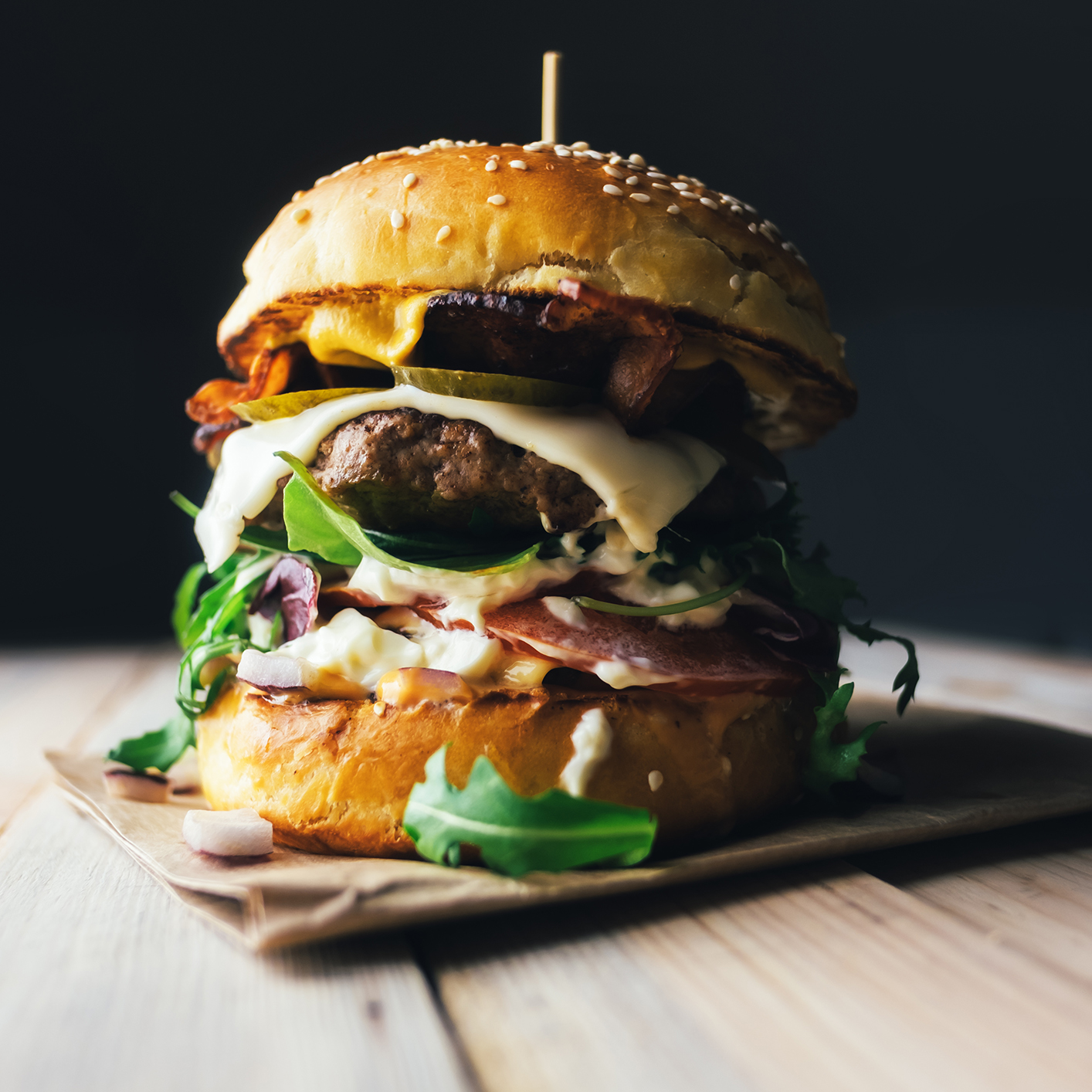 A large cheeseburger with lettuce, tomato, cheese, bacon, and sauce stacked between a sesame seed bun on a wooden table—a favorite lunch among busy Chicago lawyers.