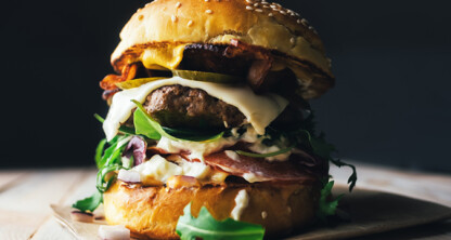 A close-up of a loaded hamburger with lettuce, pickles, cheese, bacon, sauce, and a sesame seed bun on a wooden surface—perfect fuel for busy Chicago lawyers or anyone visiting law offices nearby.