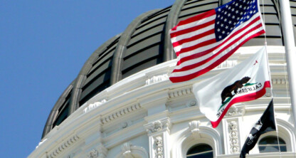 Close-up of the California State Capitol dome with the U.S., California, and POW/MIA flags flying at half-staff against a clear blue sky—an inspiring sight for chicago lawyers seeking litigation support and justice.