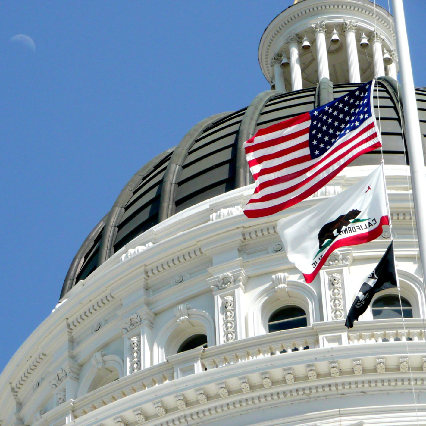 Close-up of the California State Capitol dome with the U.S., California, and POW/MIA flags flying at half-staff against a clear blue sky—an inspiring sight for chicago lawyers seeking litigation support and justice.