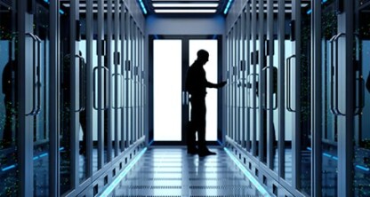 A person stands in a brightly lit corridor between rows of server racks in a data center, working on equipment—a scene reminiscent of the high-security environments found in corporate law offices specializing in intellectual property law.