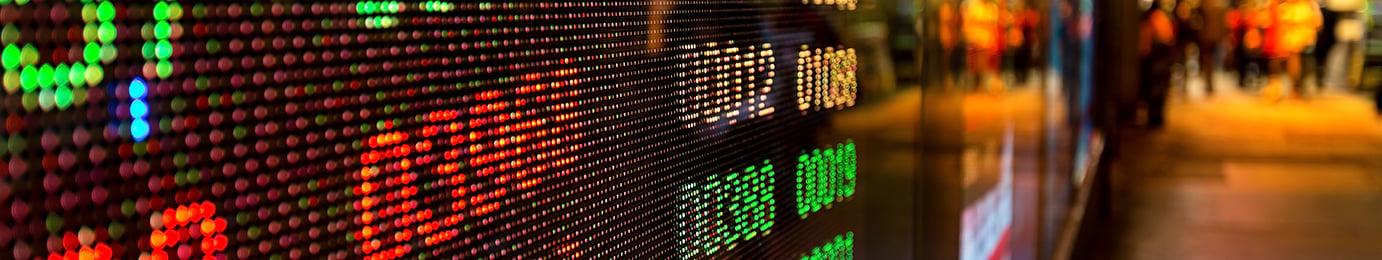 A digital stock market display shows rows of colorful numbers and graphs, with a blurred urban street scene in the background—capturing the fast-paced world outside a corporate law office.