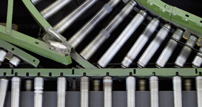 Close-up view of a conveyor system with green metal supports and silver rollers, with yellow packages in motion—a scene typical in law offices managing high-volume legal documents for intellectual property law cases.