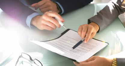 Two people in business attire review and discuss a document on a clipboard at a glass desk, providing litigation support for law offices, with eyeglasses placed nearby.