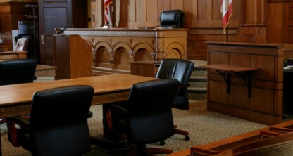 Empty courtroom with wooden benches, tables, chairs, a judge's bench, and American flags; no people present—an atmosphere where Chicago lawyers might debate intellectual property law.