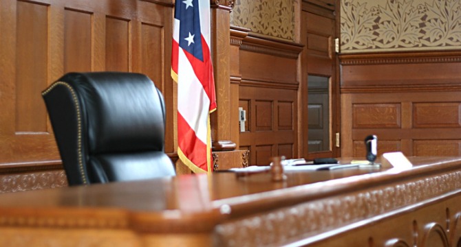 An empty judge's bench in a courtroom, with an American flag in the background and a wooden interior, echoes the solemn atmosphere found in many law offices specializing in intellectual property law.