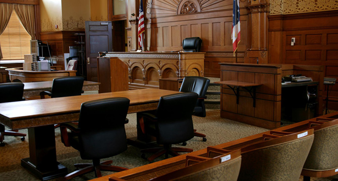 Empty courtroom with wooden furnishings, judge’s bench, flags, jury box, and rows of empty chairs—an atmosphere familiar to Chicago lawyers and law offices specializing in intellectual property law.