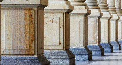 A row of large stone columns with square bases, set on a marble floor in a classical architectural style, evokes the tradition and authority often found in Chicago lawyers' offices.