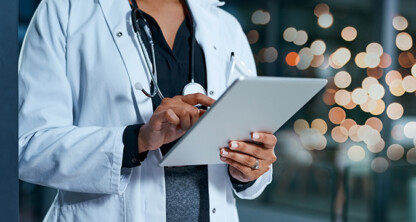 A doctor in a white coat uses a tablet, with a stethoscope around their neck and blurred lights in the background, reflecting the modern professionalism often found in Chicago lawyers and law offices.