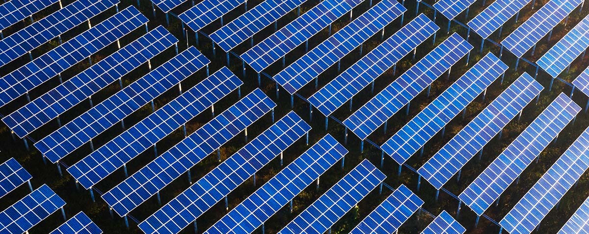 Filas de paneles solares azules dispuestos en forma de cuadrícula al aire libre, vistas desde arriba, con el logotipo de Foley &amp; Lardner LLP en la esquina inferior derecha, lo que simboliza la innovación de este bufete líder en derecho mercantil.