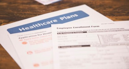 A close-up of healthcare plan documents, including an application form and an employee enrollment form, placed on a wooden surface in a law office specializing in intellectual property law.