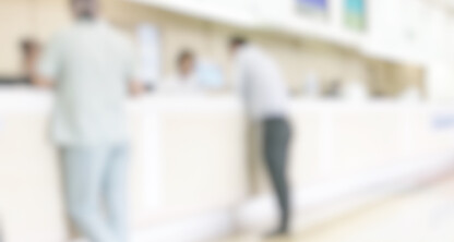 Imagen borrosa de varias personas de pie junto a un mostrador de atención al público en un espacio interior muy iluminado, posiblemente la zona de recepción de un bufete de abogados que ofrece asistencia en litigios o servicios relacionados con el derecho de la propiedad intelectual.