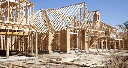 Wooden frames of houses under construction with exposed beams and plywood, set on a dirt lot under a clear blue sky—much like chicago lawyers laying the groundwork for future success.