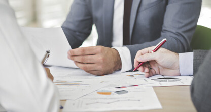 Three people in business attire at a law office table, reviewing documents and charts, discuss data and take notes—demonstrating litigation support often provided by Chicago lawyers.