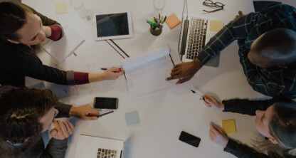 从上方俯瞰，四个人——可能是芝加哥的律师——围坐在一张白色桌子旁，手边放着笔记本电脑和文件，在现代化的办公环境中共同处理诉讼支持工作。