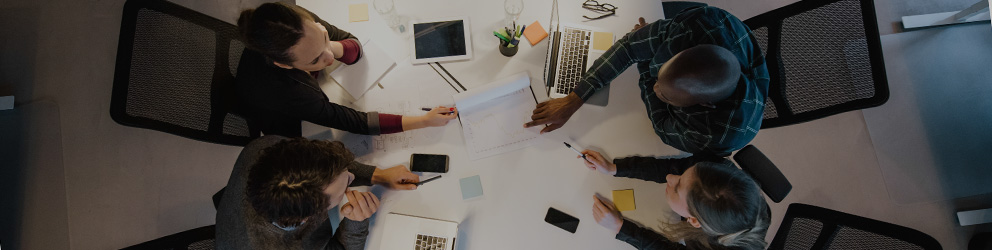 Four people, possibly lawyers in Chicago, sit around a white table with laptops and documents, collaborating on litigation support in a modern office setting, viewed from above.