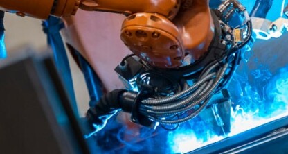 An industrial robotic arm performs automated welding on metal parts, with blue sparks and light visible in a manufacturing environment, where chicago lawyers provide litigation support for machinery compliance.