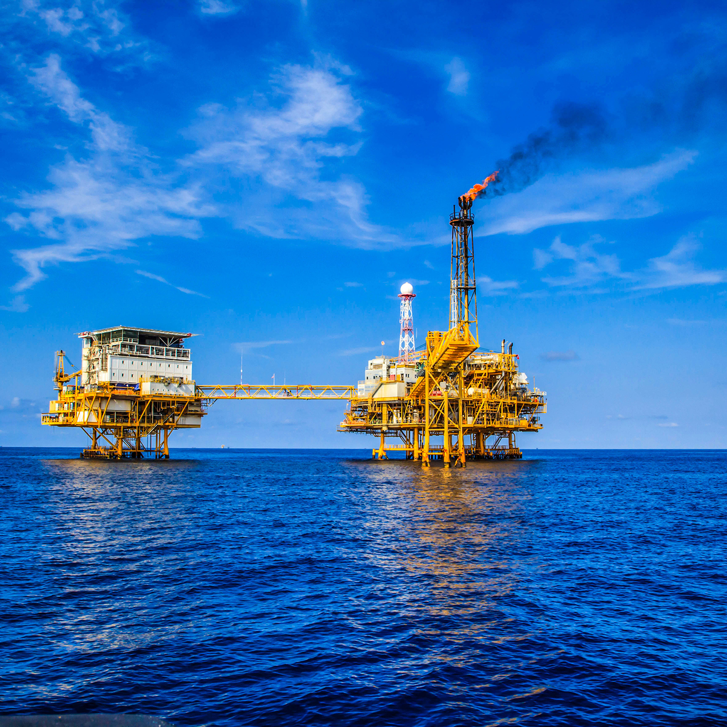 Offshore oil platform with a flare stack emitting smoke, situated in the ocean under a clear blue sky—an image often referenced by corporate law office teams and lawyers in Chicago handling complex maritime regulations.