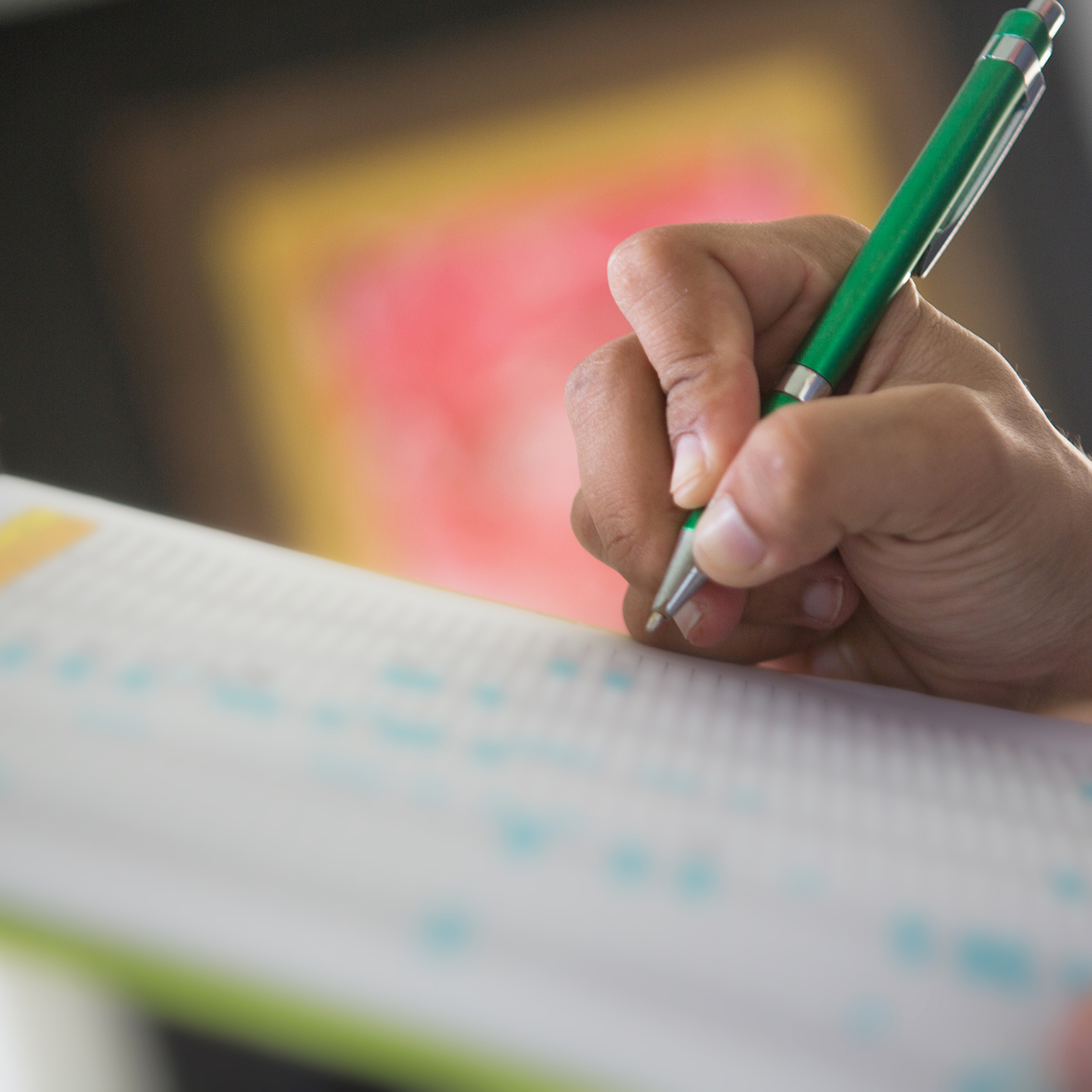A person holds a green pen and writes on a sheet of paper with a chart or grid pattern, perhaps drafting documents in one of the law offices frequented by top chicago lawyers, with a blurred background.