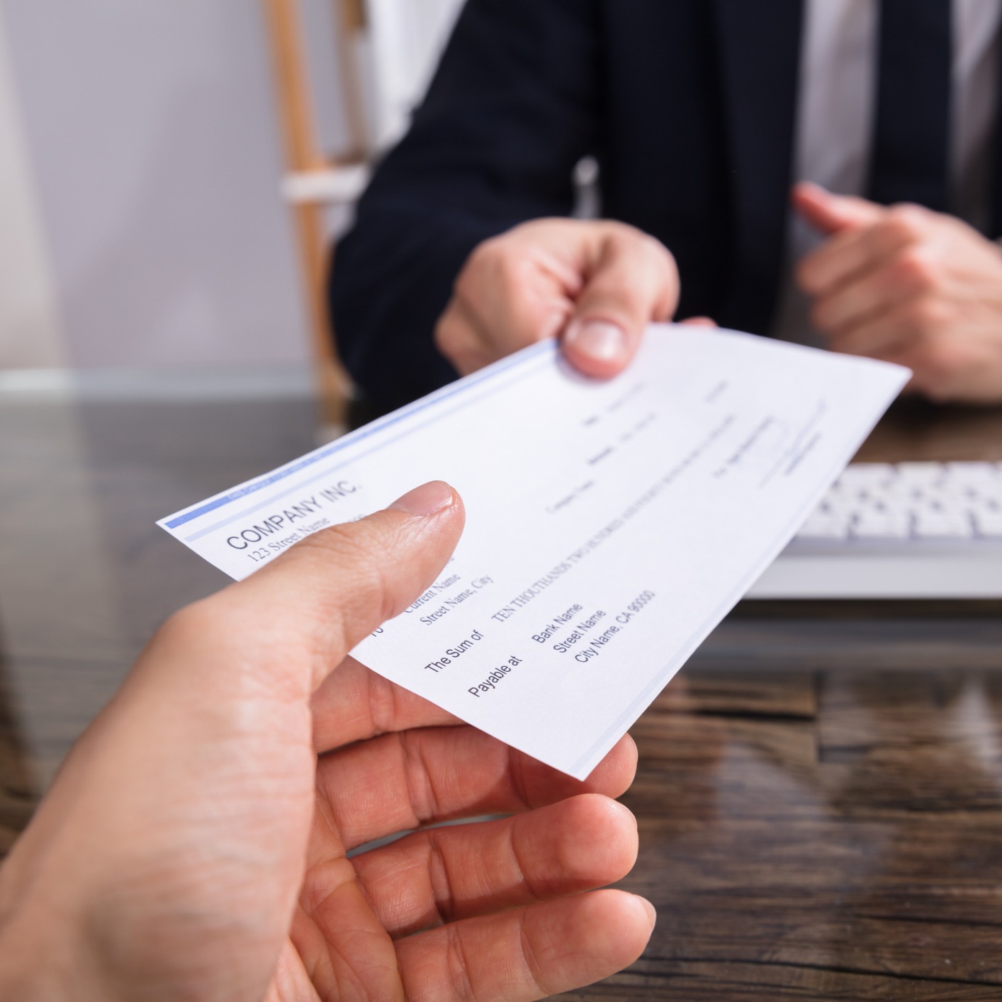 A person hands a check to another across a desk in a professional office setting, highlighting the financial transactions often seen in law offices providing litigation support.