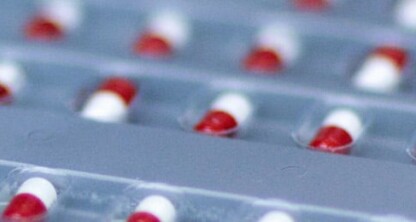Varias filas de cápsulas rojas y blancas se presentan en envases blíster de plástico transparente, listas para su distribución por parte de un bufete de abogados líder especializado en derecho de la propiedad intelectual.