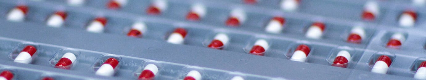 Varias filas de cápsulas rojas y blancas se presentan en envases blíster de plástico transparente, listas para su distribución por parte de un bufete de abogados líder especializado en derecho de la propiedad intelectual.