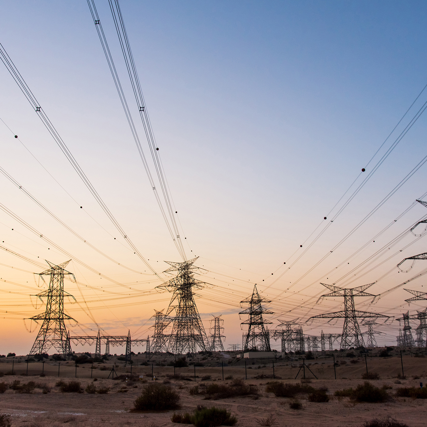 Multiple high-voltage power transmission towers and wires stretch across a dry, open landscape at sunset, evoking the interconnected strength found in leading law offices and lawyers in Chicago.
