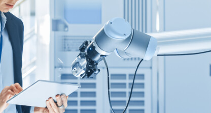 A woman in business attire uses a digital tablet next to a robotic arm in a modern lab, reflecting the intersection of technology and intellectual property law in innovative industries.