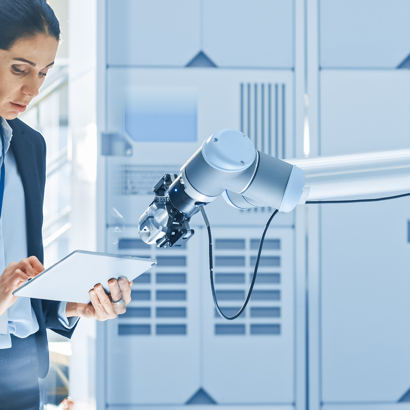A woman in business attire uses a digital tablet next to a robotic arm in a modern lab, reflecting the intersection of technology and intellectual property law in innovative industries.
