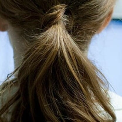 Eine Person mit braunem Haar, das zu einem Pferdeschwanz gebunden ist, sitzt vor einem Computermonitor in einem hellen Innenraum, wie er für moderne Anwaltskanzleien typisch ist.