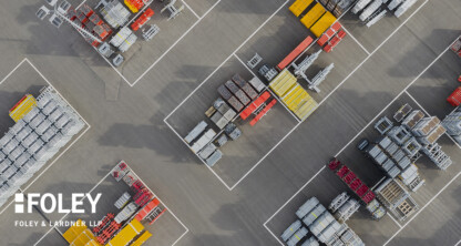 Aerial view of an industrial storage yard with organized stacks of metal and construction materials, outlined by white boundary lines. The Foley & Lardner LLP logo, known for its intellectual property law expertise, appears in the lower left corner.