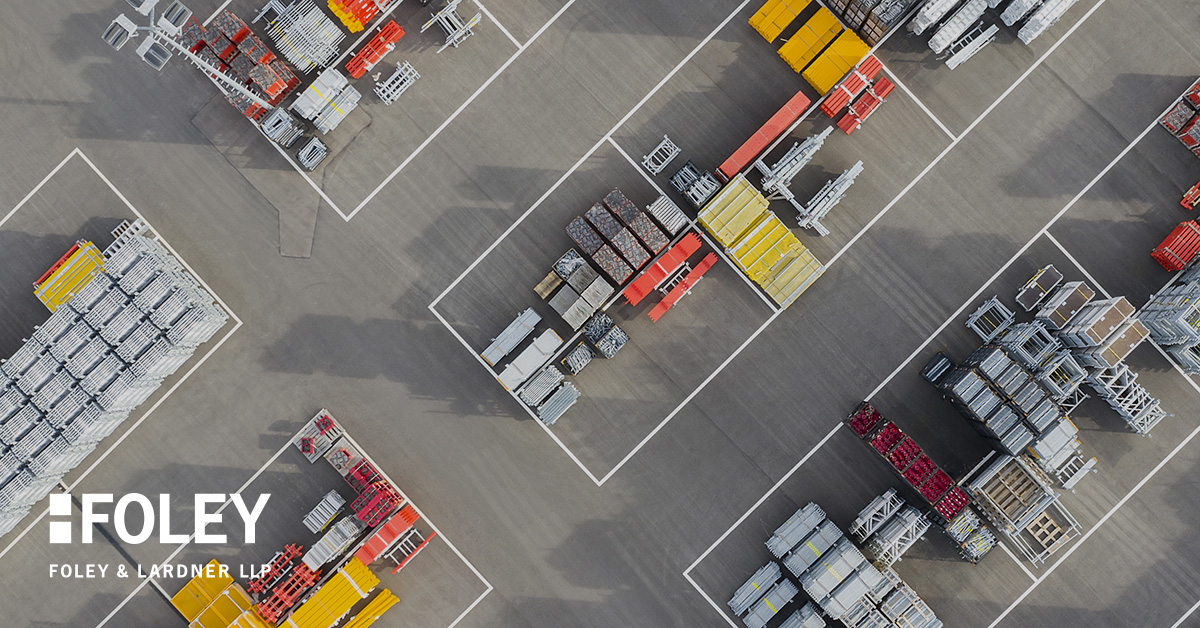 Aerial view of an industrial storage yard with organized stacks of metal and construction materials, outlined by white boundary lines. The Foley & Lardner LLP logo, known for its intellectual property law expertise, appears in the lower left corner.