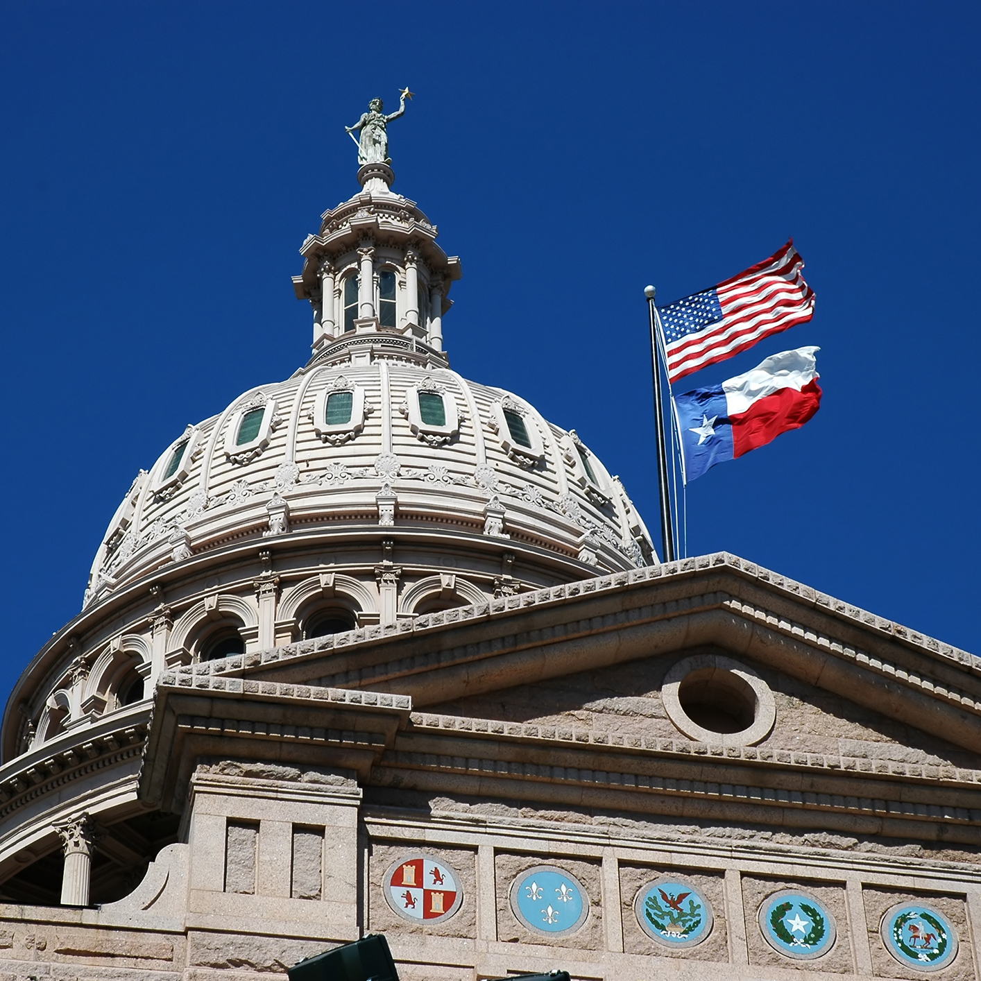 The dome of a government building with American and Texas flags flying, set against a clear blue sky, evokes the dignified presence of prominent law offices handling important matters of justice and governance.