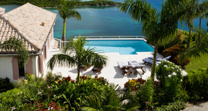 A villa with a tiled roof overlooks a pool, palm trees, and tropical landscaping, offering tranquil views—perfect for a corporate law office retreat or inspiration for those specializing in intellectual property law.