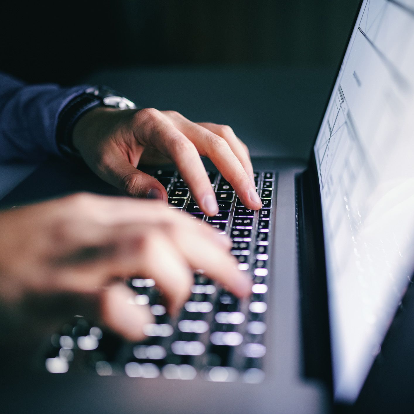 Close-up of hands typing on a laptop keyboard in a corporate law office, with the screen partially visible and the background blurred.