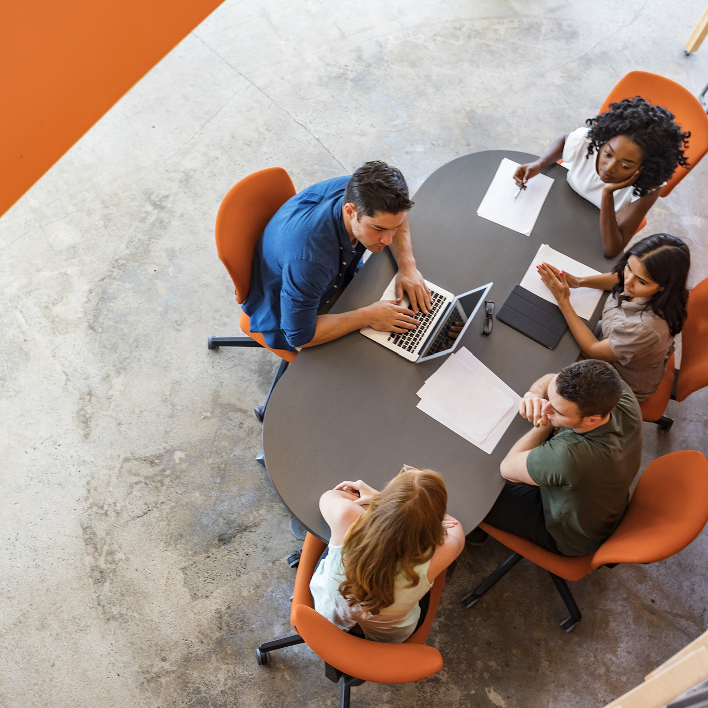 Four people sit around an oval table with papers, a laptop, and notepads, engaged in a meeting or group discussion about intellectual property law in a modern law office setting.