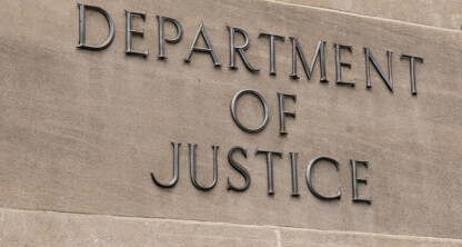 The words "Department of Justice" are mounted on a beige stone wall, reflecting the institution’s crucial role in areas like intellectual property law and litigation support.