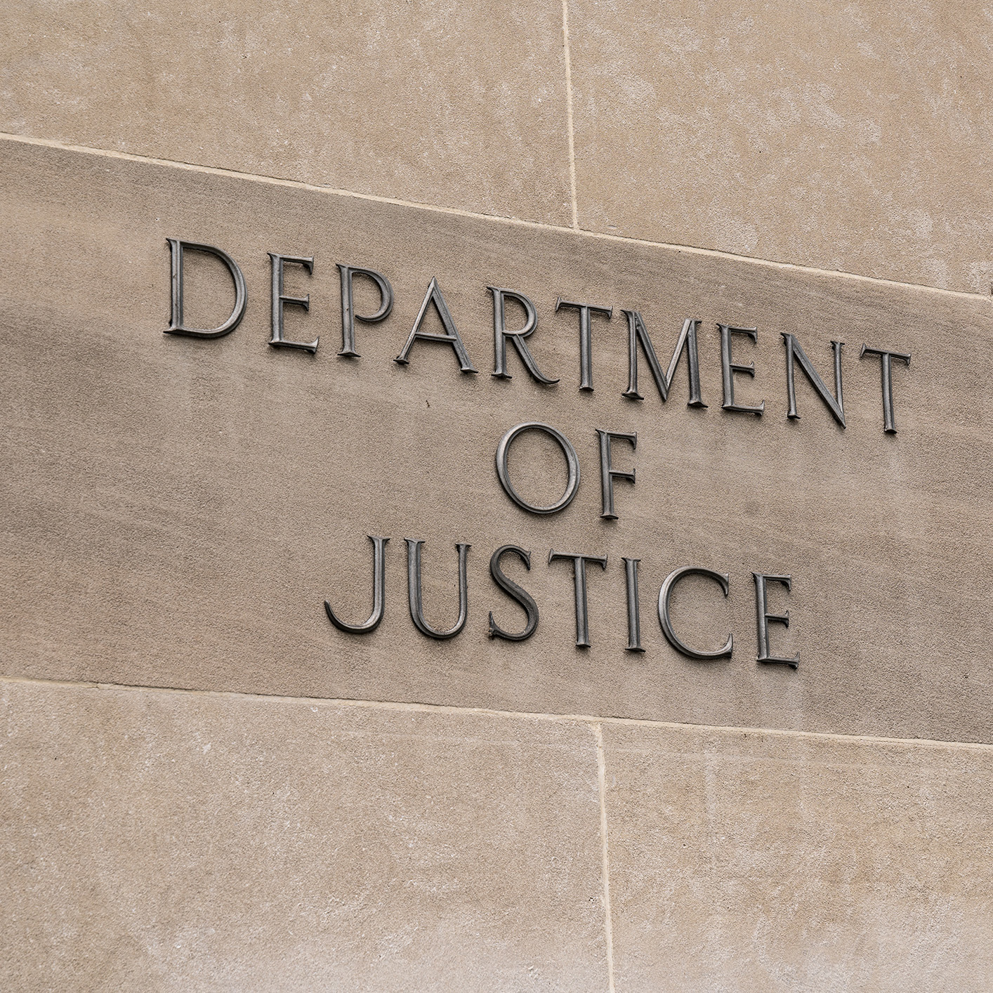 The words "Department of Justice" are mounted on a beige stone wall, reflecting the institution’s crucial role in areas like intellectual property law and litigation support.