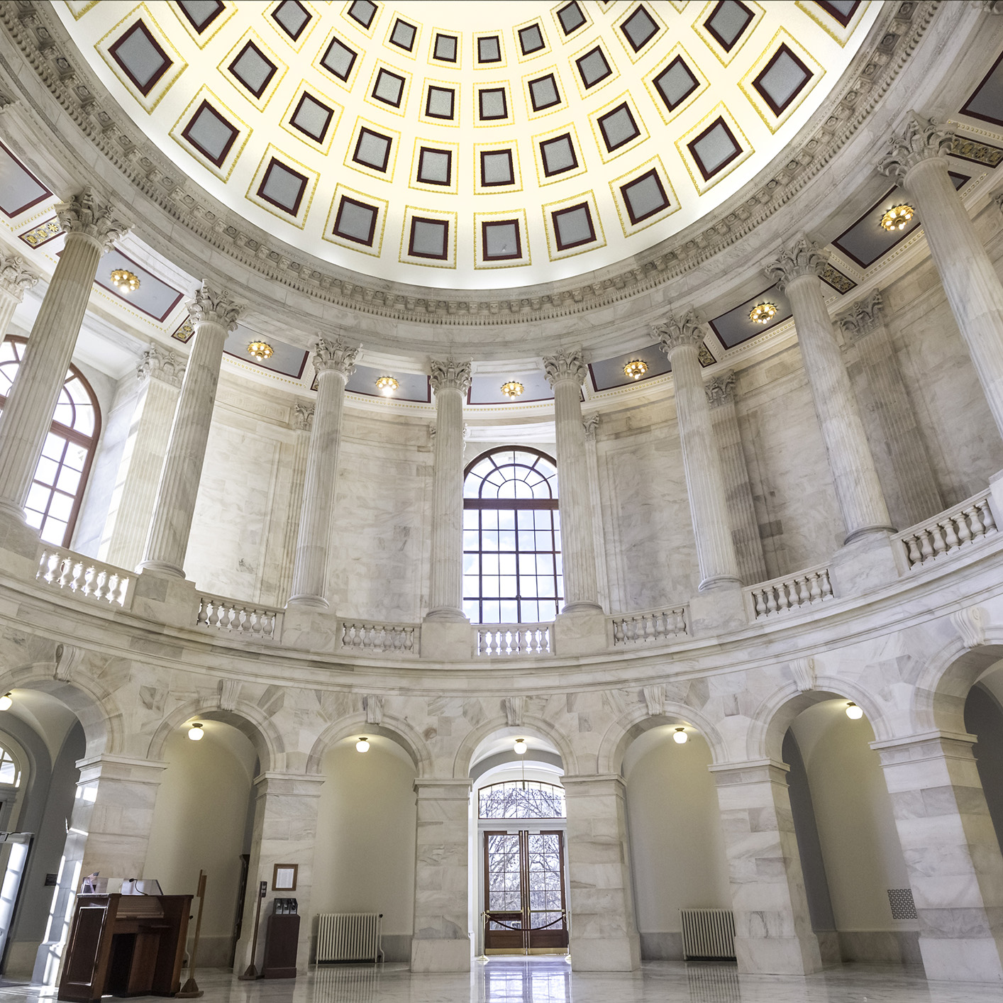 Grand interior of a domed rotunda with marble columns, arched windows, and geometric ceiling pattern—an impressive setting often found in prestigious law offices or a corporate law office in Chicago. Natural light filters through large glass doors and windows.