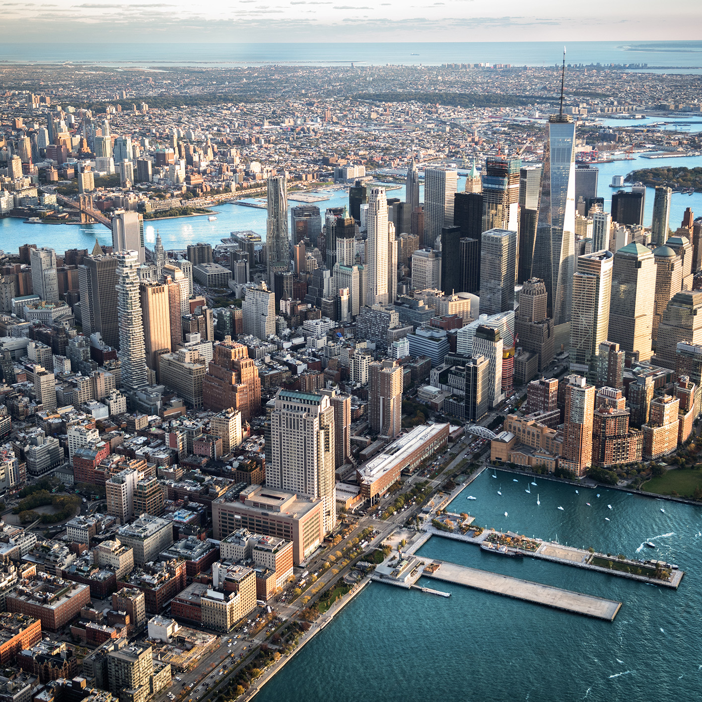 Aerial view of Lower Manhattan, New York City, showcasing tall skyscrapers, bustling waterfront, and surrounding rivers—home to many leading corporate law offices under a partly cloudy sky.