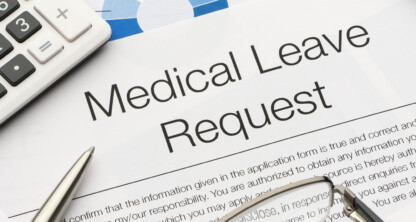 Formulario de solicitud de baja médica sobre una mesa en un despacho de abogados corporativos, con un bolígrafo, gafas, calculadora y documentos financieros al fondo.