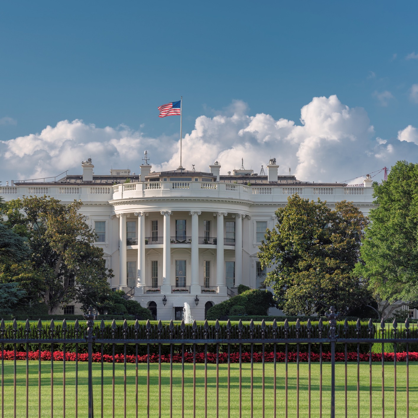 The White House in Washington, D.C., with an American flag flying atop, framed by trees and a black iron fence—a symbol recognized by law offices and chicago lawyers specializing in intellectual property law.