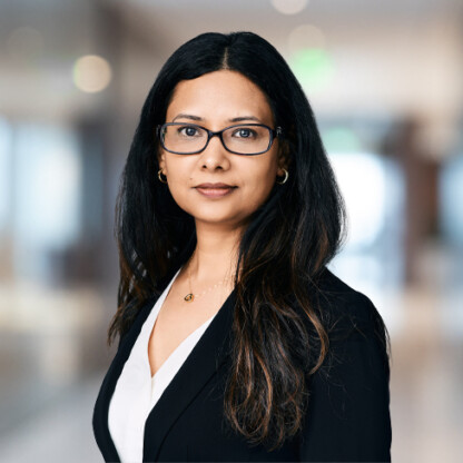 Woman with long dark hair and glasses, wearing a black blazer and white blouse, stands in a law office hallway—a confident presence among Chicago lawyers specializing in intellectual property law.