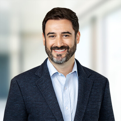 Man with dark hair and beard wearing a blue blazer and light shirt, smiling in a bright, blurred indoor setting—ideal for a corporate law office or lawyers in Chicago seeking a professional look.